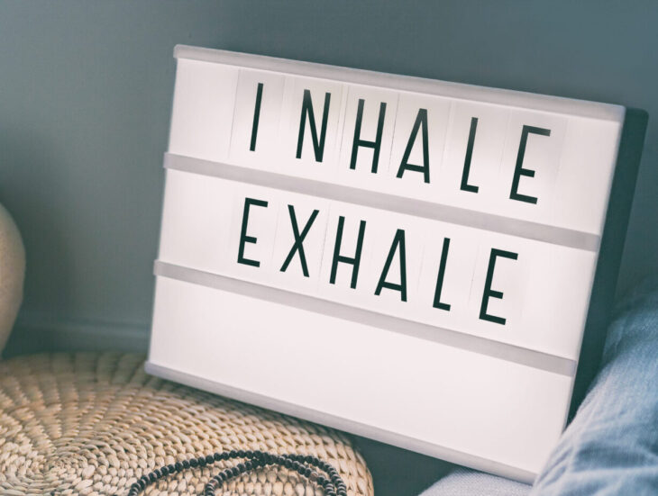 Yoga breathing INHALE EXHALE sign at fitness class on lightbox inspirational message with exercise mat, mala beads, meditation pillow. Accessories for fit home lifestyle.