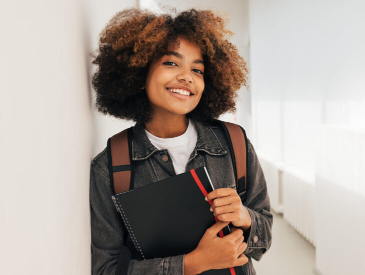 Portrait of a beautiful female college student leaning a wall and looking at camera